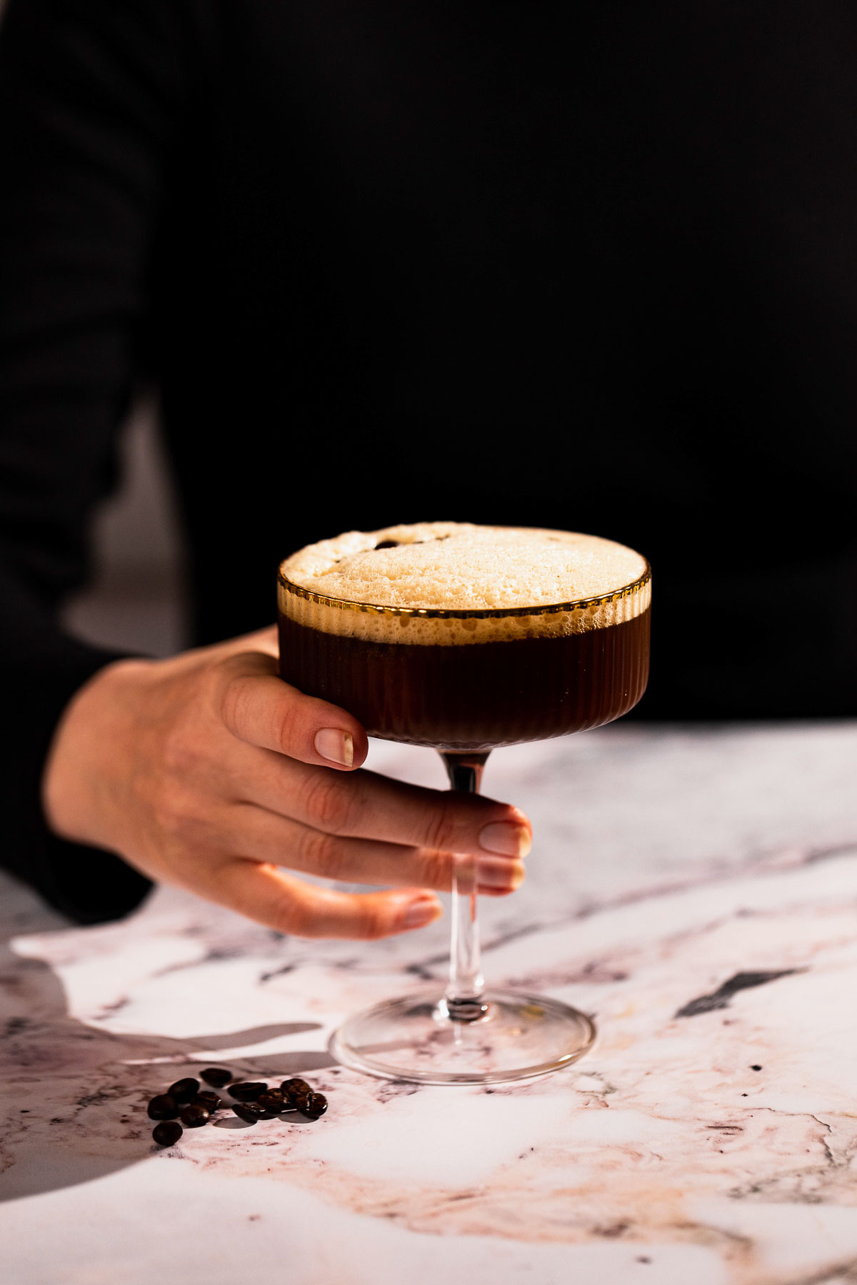 Hand holding stem of a carajillo in a cocktail glass.