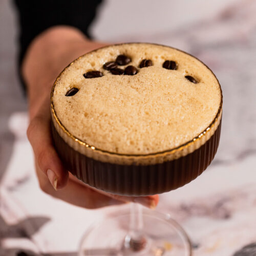 Carajillo drink in a cocktail glass with a hand holding it.