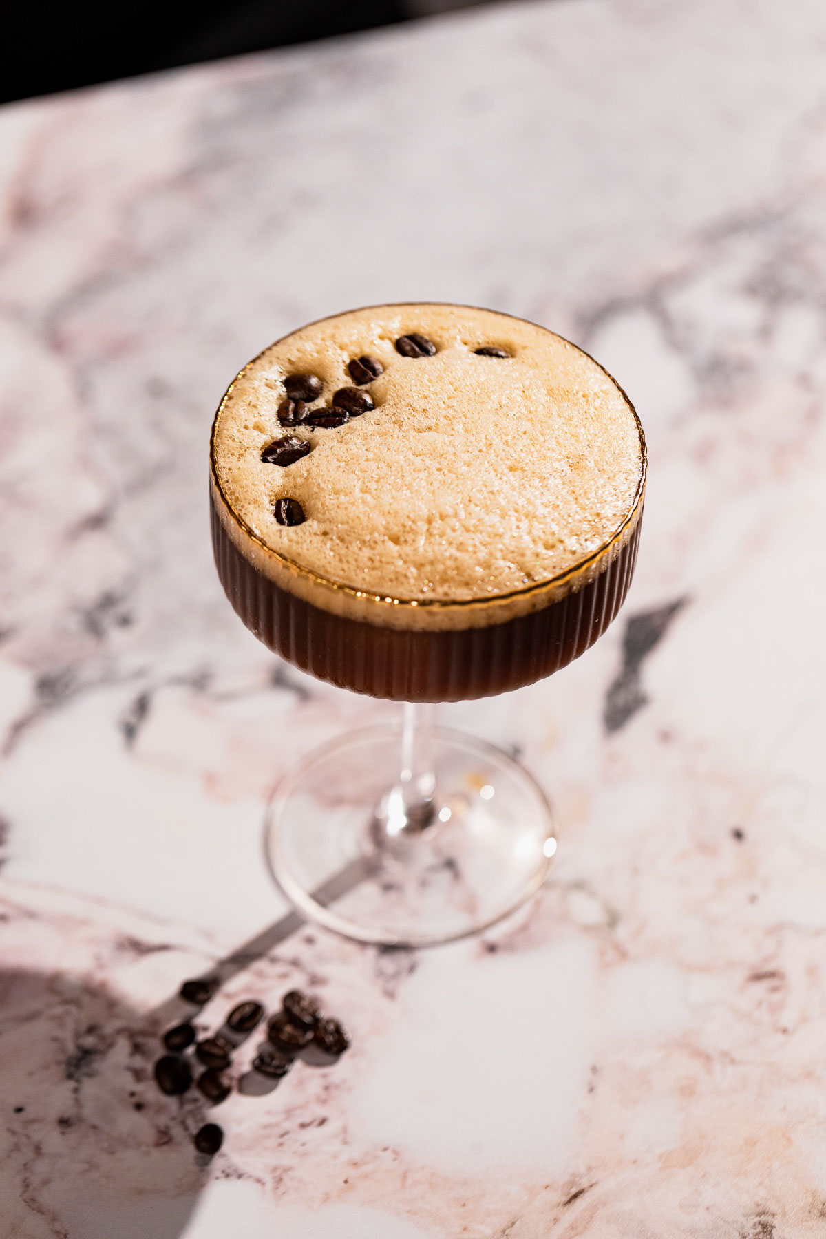 Top of a frothy carajillo cocktail with espresso beans on top.