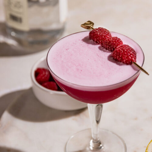 Clover club cocktail garnished with fresh raspberries and frothy egg white top.