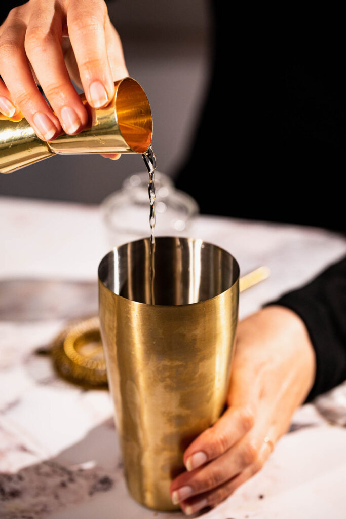 Hand pouring rum into cocktail shaker.