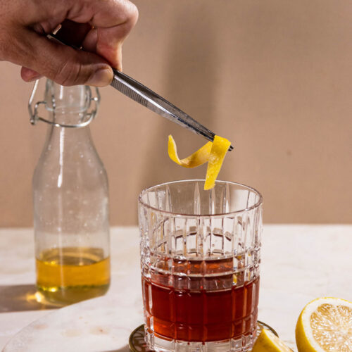 Sazerac cocktail with a lemon twist being added.