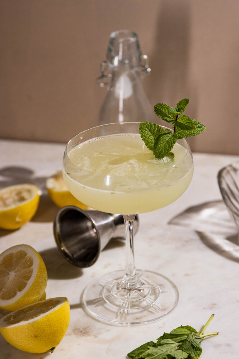 Southside cocktail with mint sprig on a table with squeezed lemons.