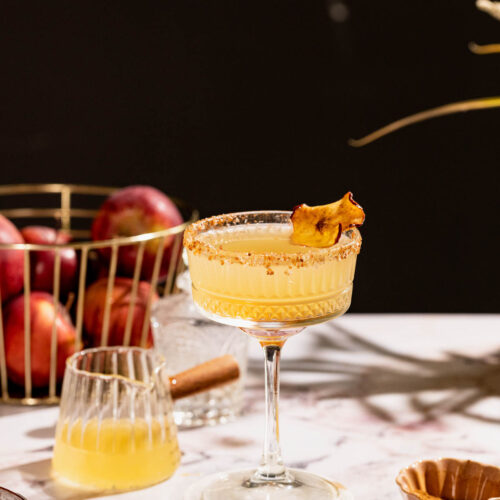 Apple cider margarita in a cocktail glass on a table with apples.