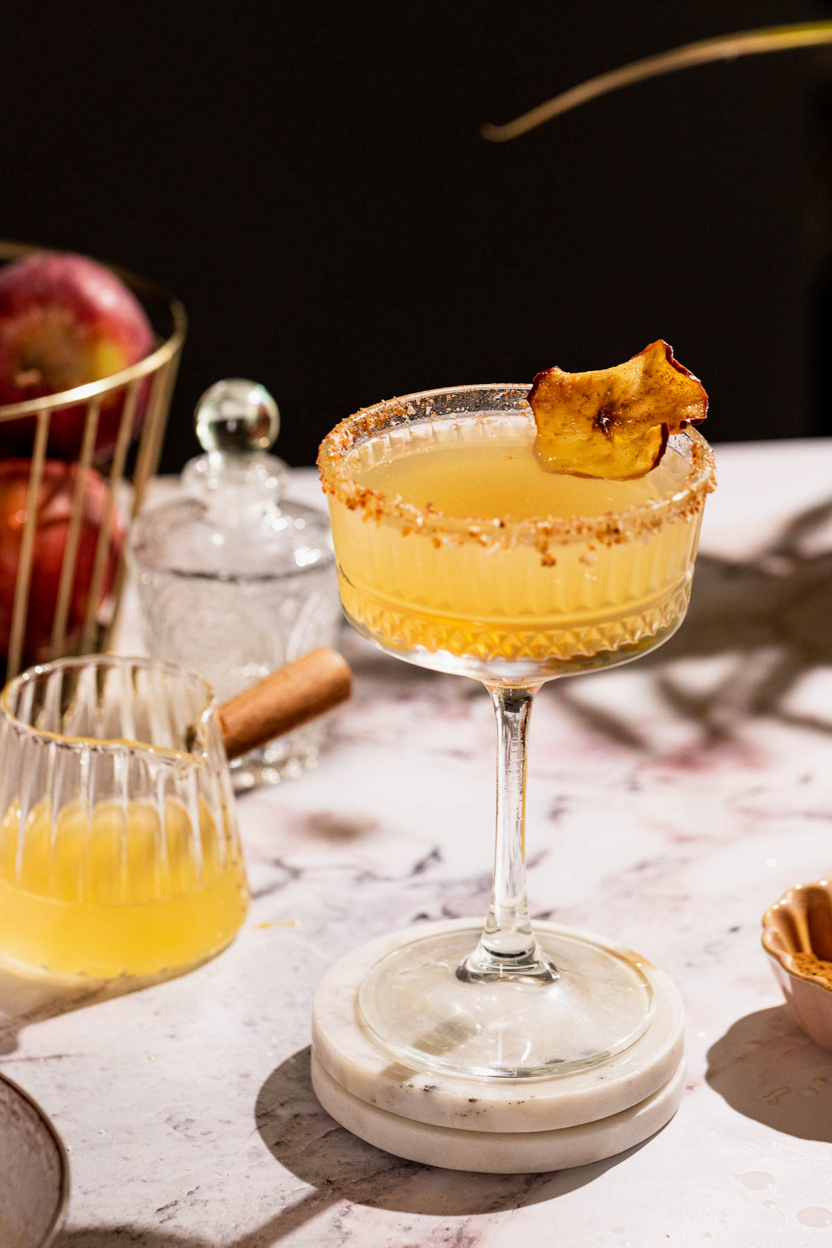 Apple cider margarita on a white surface with apples in the background.