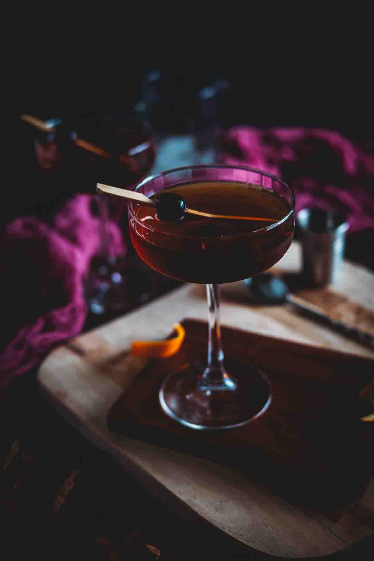 Three quarter shot looking into a coup glass holding an amber smoked manhattan cocktail.