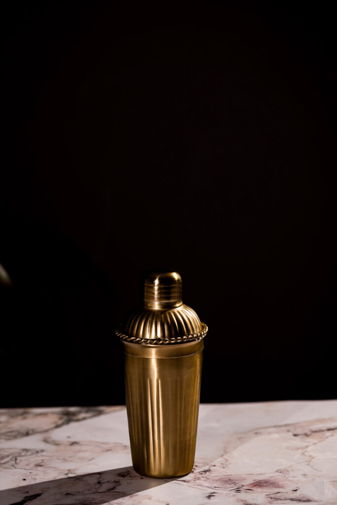 A gold cocktail shaker rests on a marble surface with a dark background.