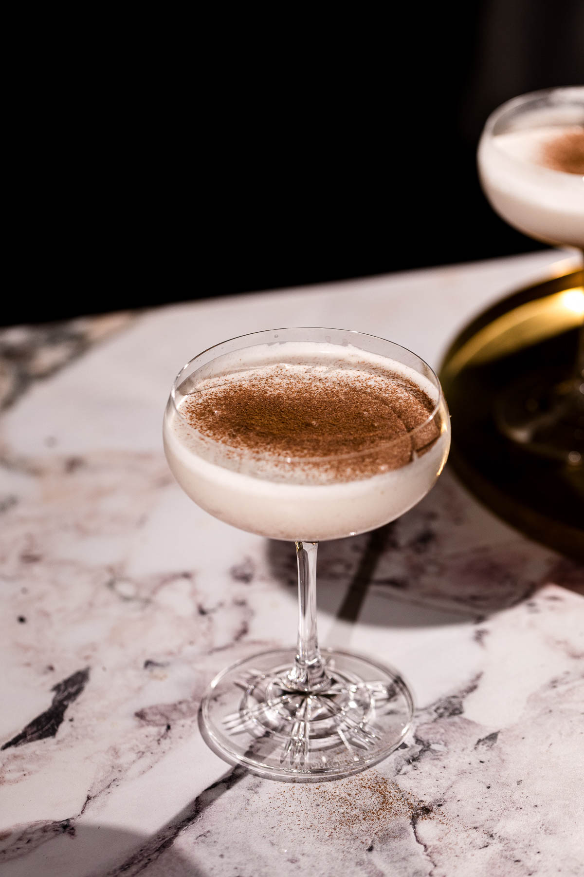 A creamy eggnog martini and topped with cinnamon sits on a marbled surface.