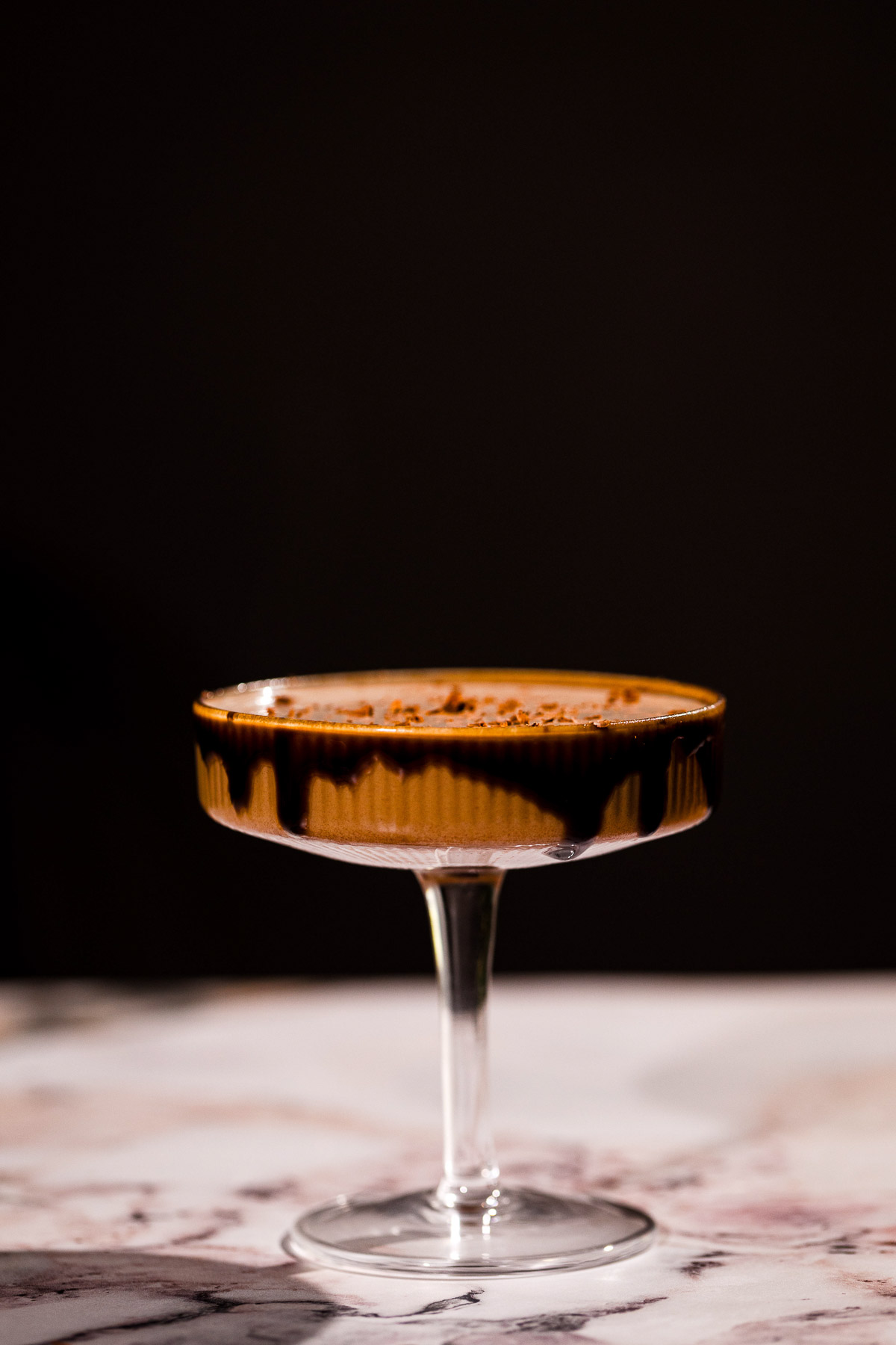 A chocolate martini sits in a coupe glass on a marble surface against a dark background.