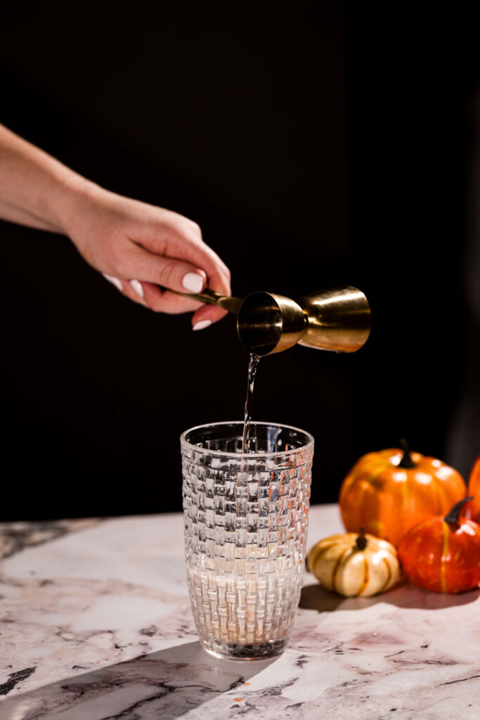 Vodka pouring from jigger into a cocktail shaker.