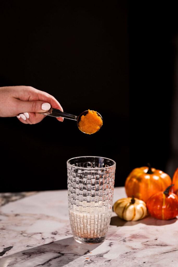 Spoonful of leftover pumpkin pie being dropped into a cocktail shaker.