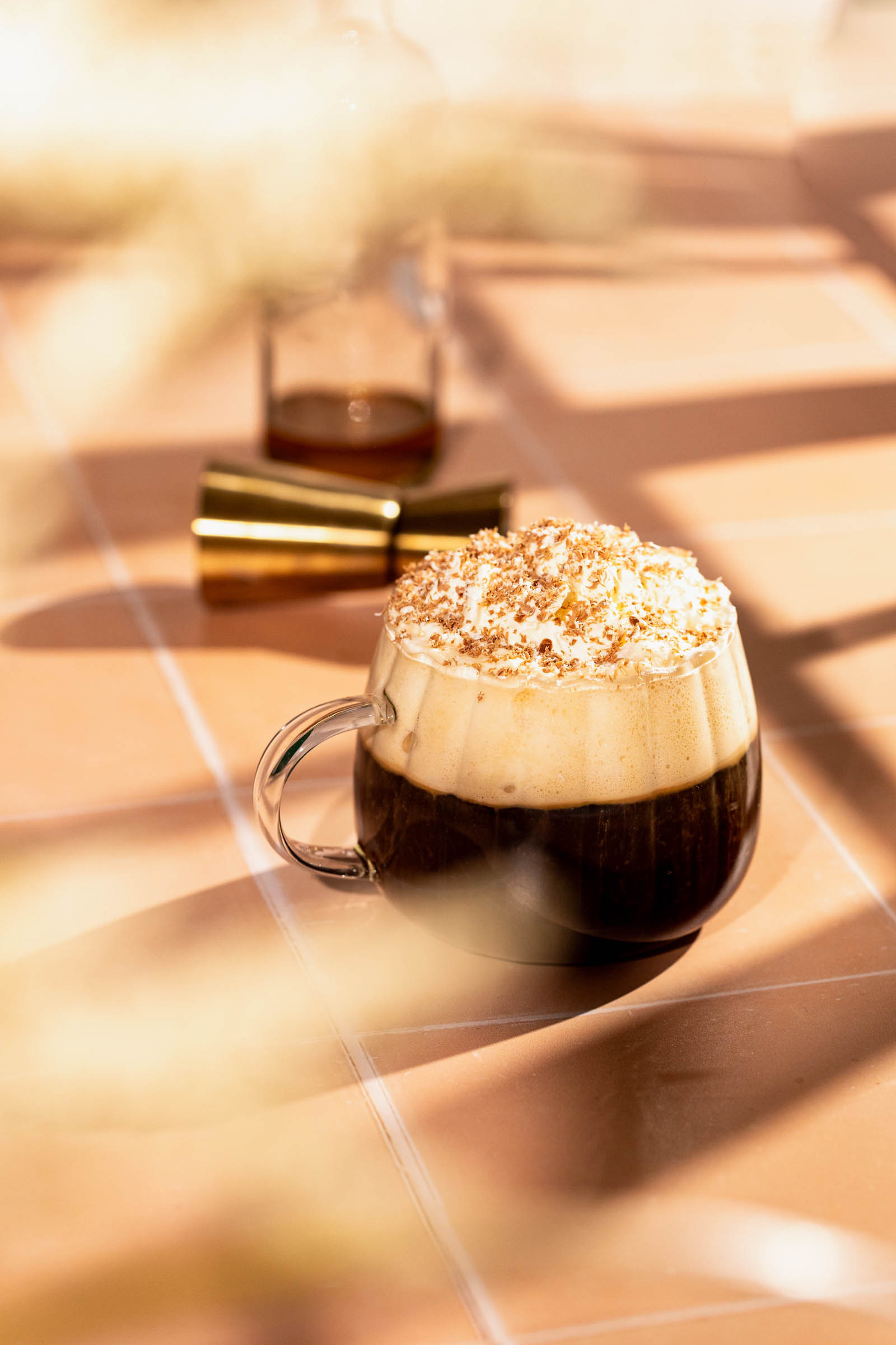 A mug of frothy Cafe Caribbean with whipped cream and sprinkles sits on a sunlit tiled surface.