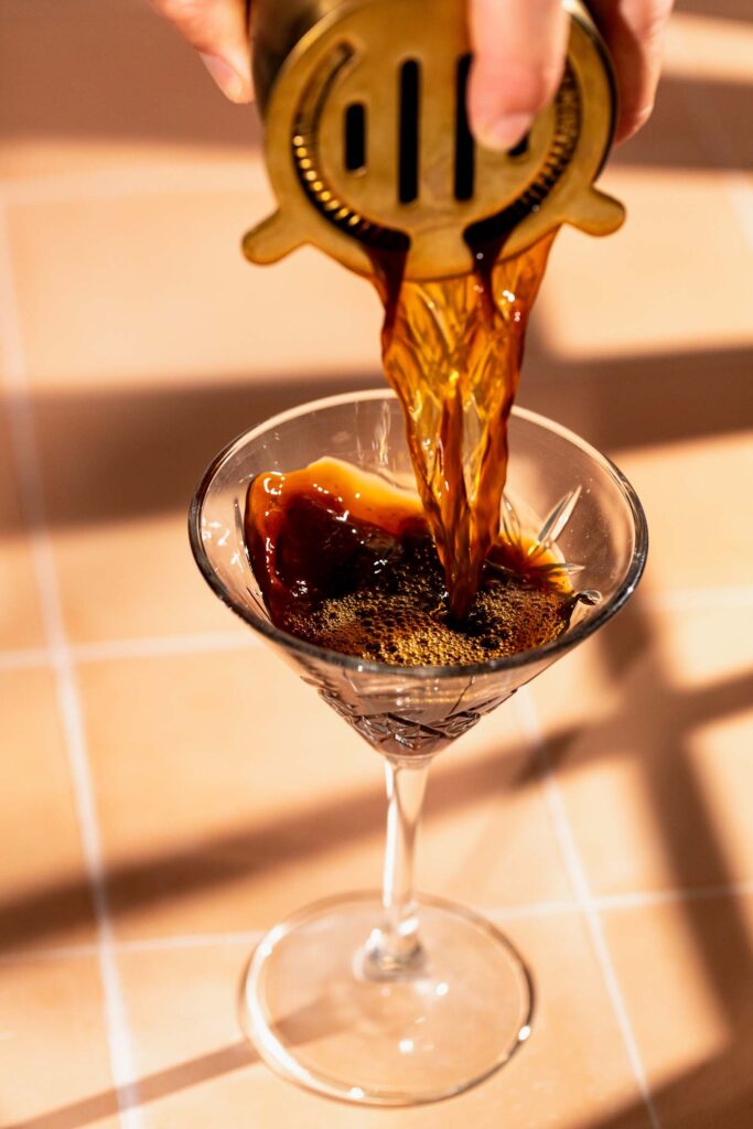 Espresso martini being poured through a strainer.