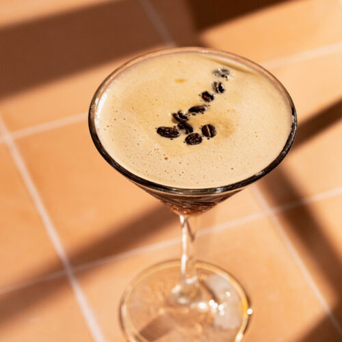 Espresso martini in a glass with a frothy top and coffee beans as a garnish.