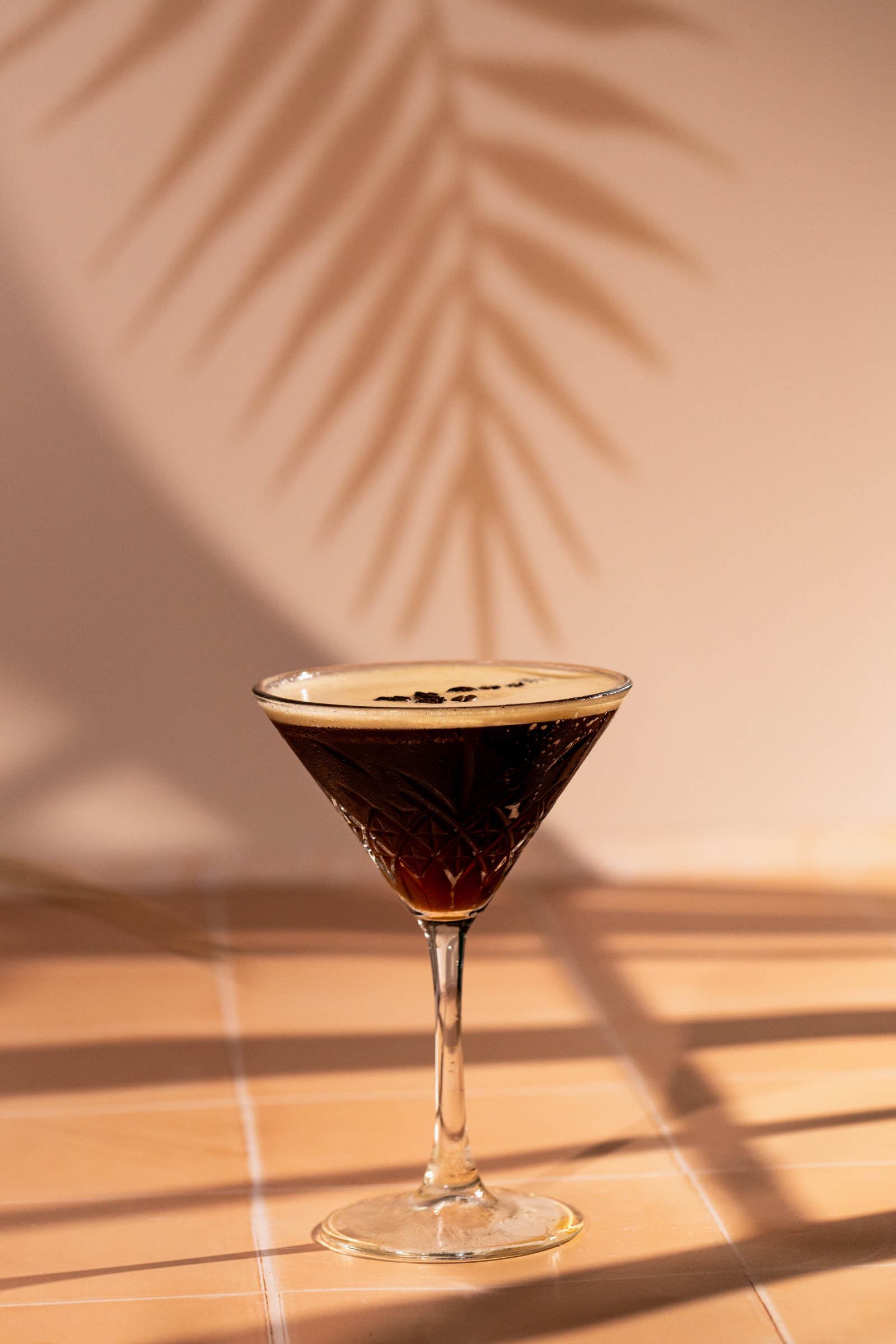 Side show of an espresso martini in a martini glass with light and plant shadows in the background.