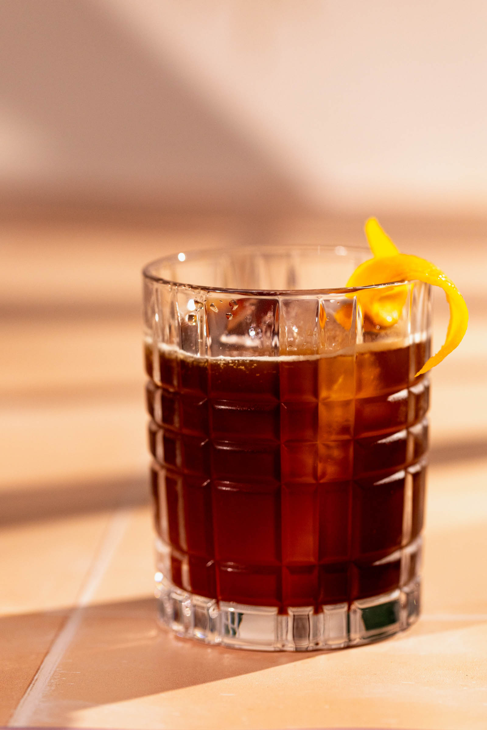 An espresso old fashioned with an orange peel twist on a tiled surface.