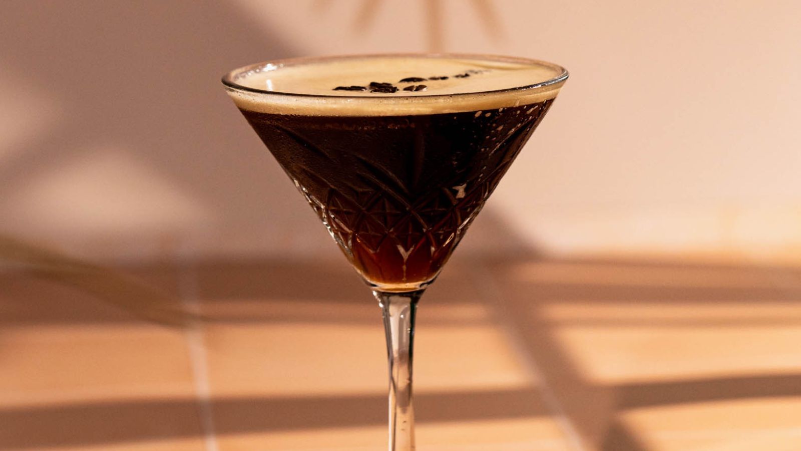 A glass of dark espresso martini with creamy foam and coffee bean garnish against a neutral background.