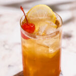 A glass of iced tea with a lemon slice and cherry sits on a marble surface.