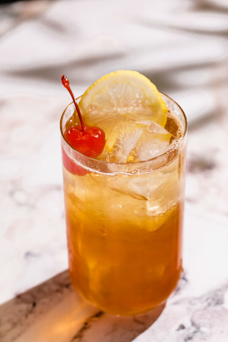 A glass of iced tea with a lemon slice and cherry sits on a marble surface.