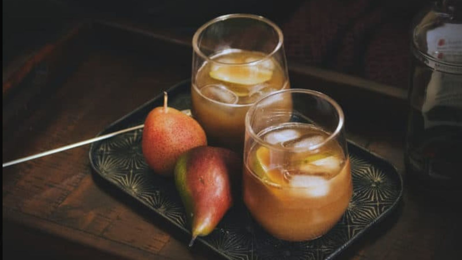 On a tray are two glasses of iced tea with lemon slices and two red pears.