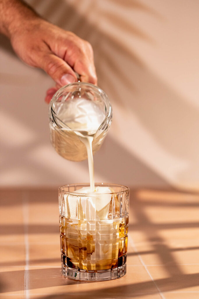 Cream is poured from a small glass over Kahlua.