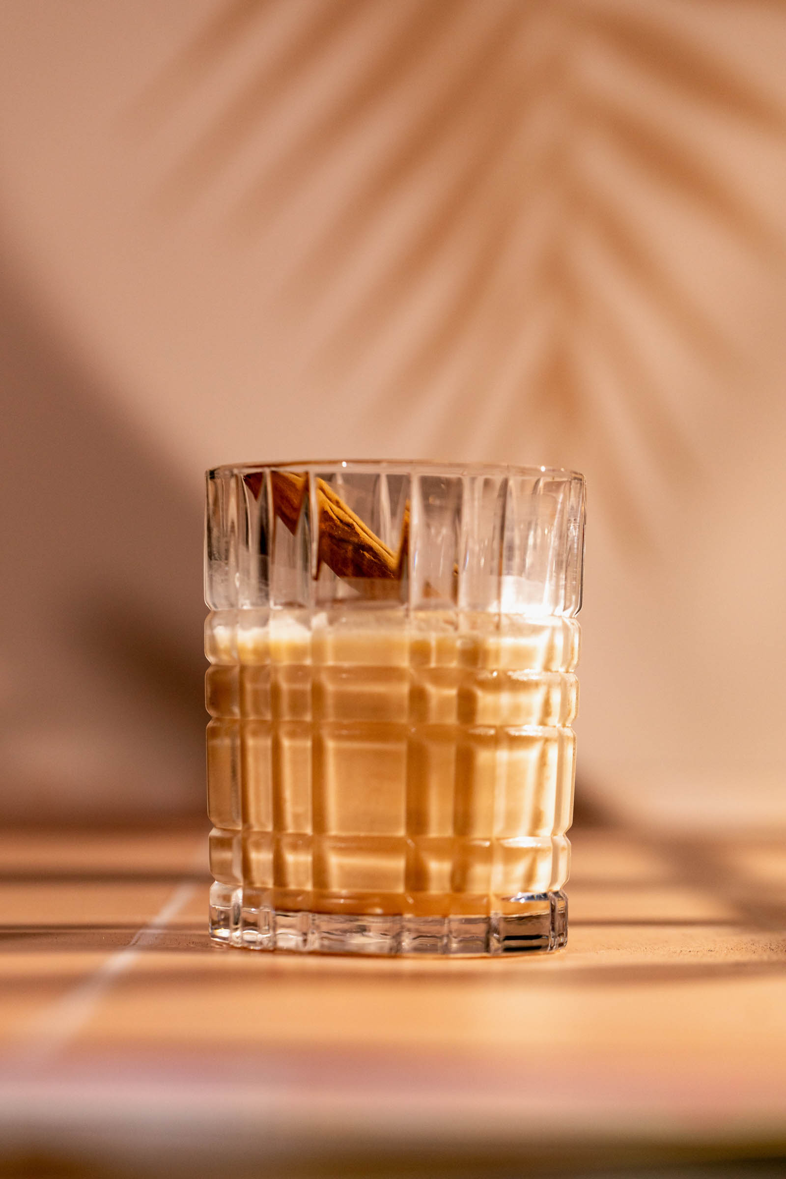 A white russian sits on a table in warm lighting, casting a decorative leaf shadow in the background.