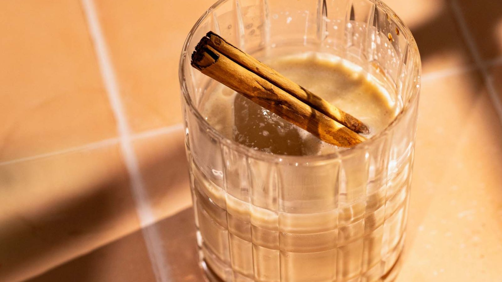 A glass of iced coffee with cream, garnished with a cinnamon stick.