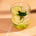 A Caipirinha garnished with lime and mint sits on a tiled surface.
