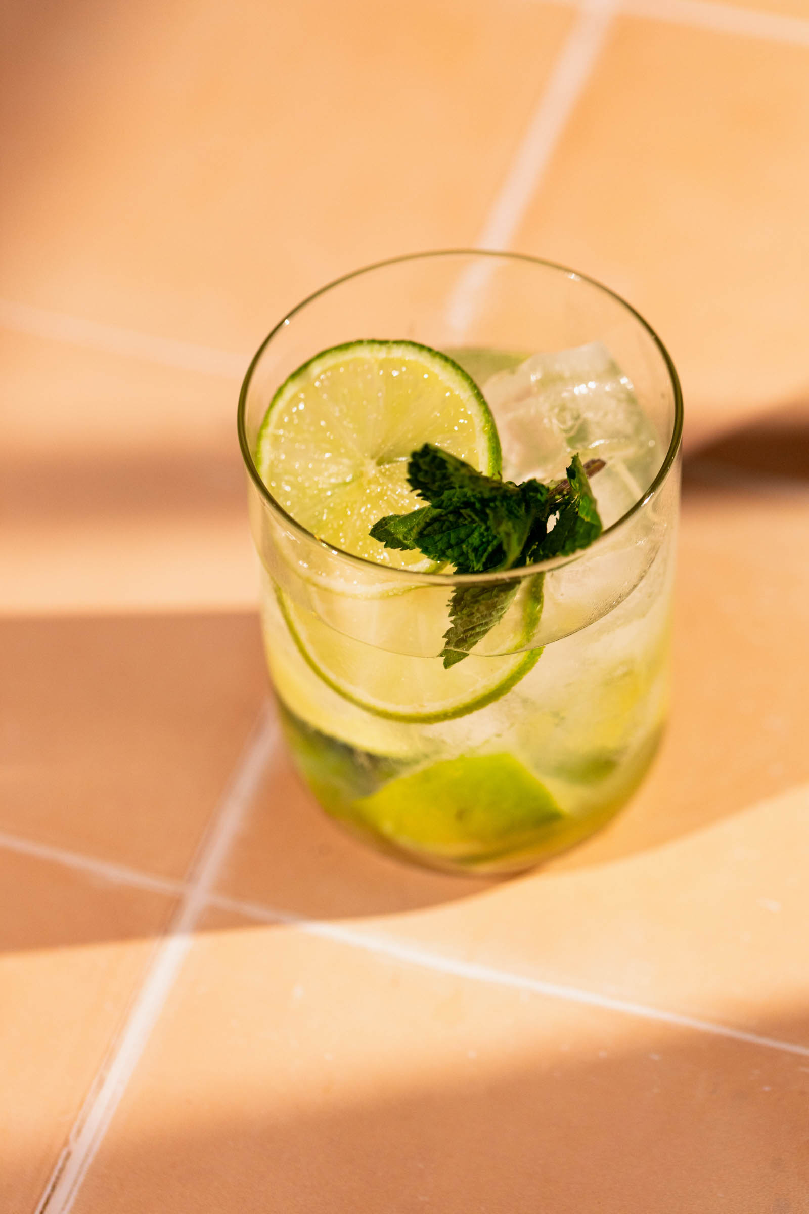 A Caipirinha garnished with lime and mint sits on a tiled surface.