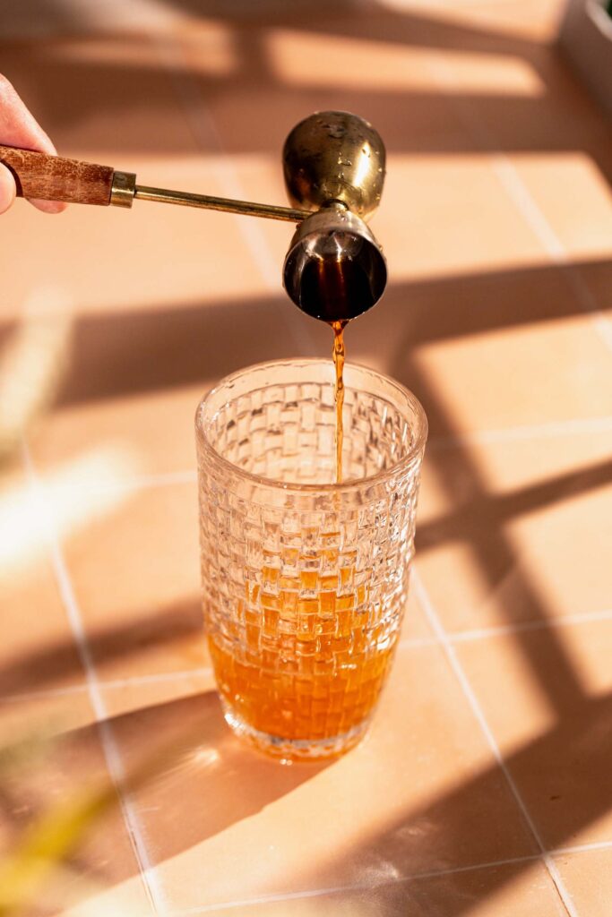 Sunlight casts shadows on a tiled surface as Chambord pours into a textured glass.