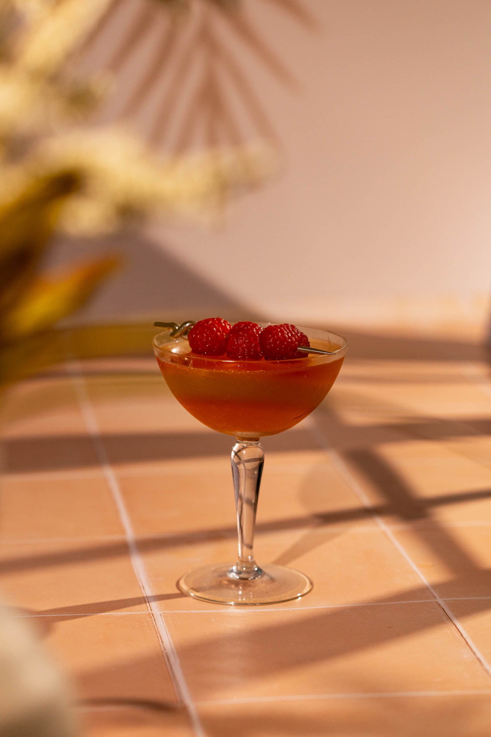 A French Martini cocktail garnished with three raspberries rests on a warmly lit tiled surface.