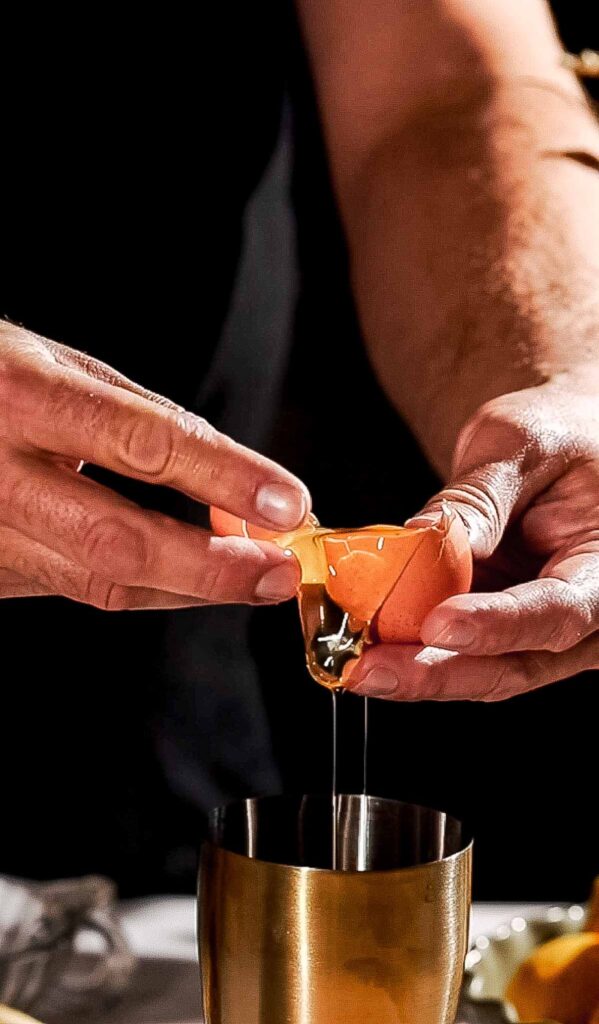 A man cracks an egg over a metal container, allowing the white to flow in.