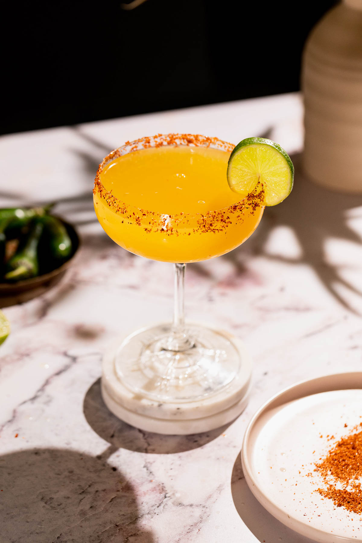 A spicy mango margarita cocktail with a chili-rimmed glass and lime slice garnish sits on a marble surface.