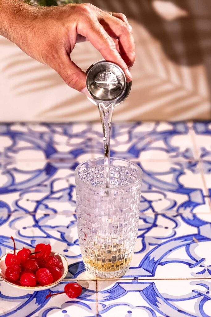 White Rum is poured into a textured cocktail shaker on a blue and white tiled surface.