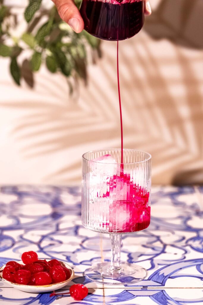 Grenadine being poured into a ice filled cocktail glass.