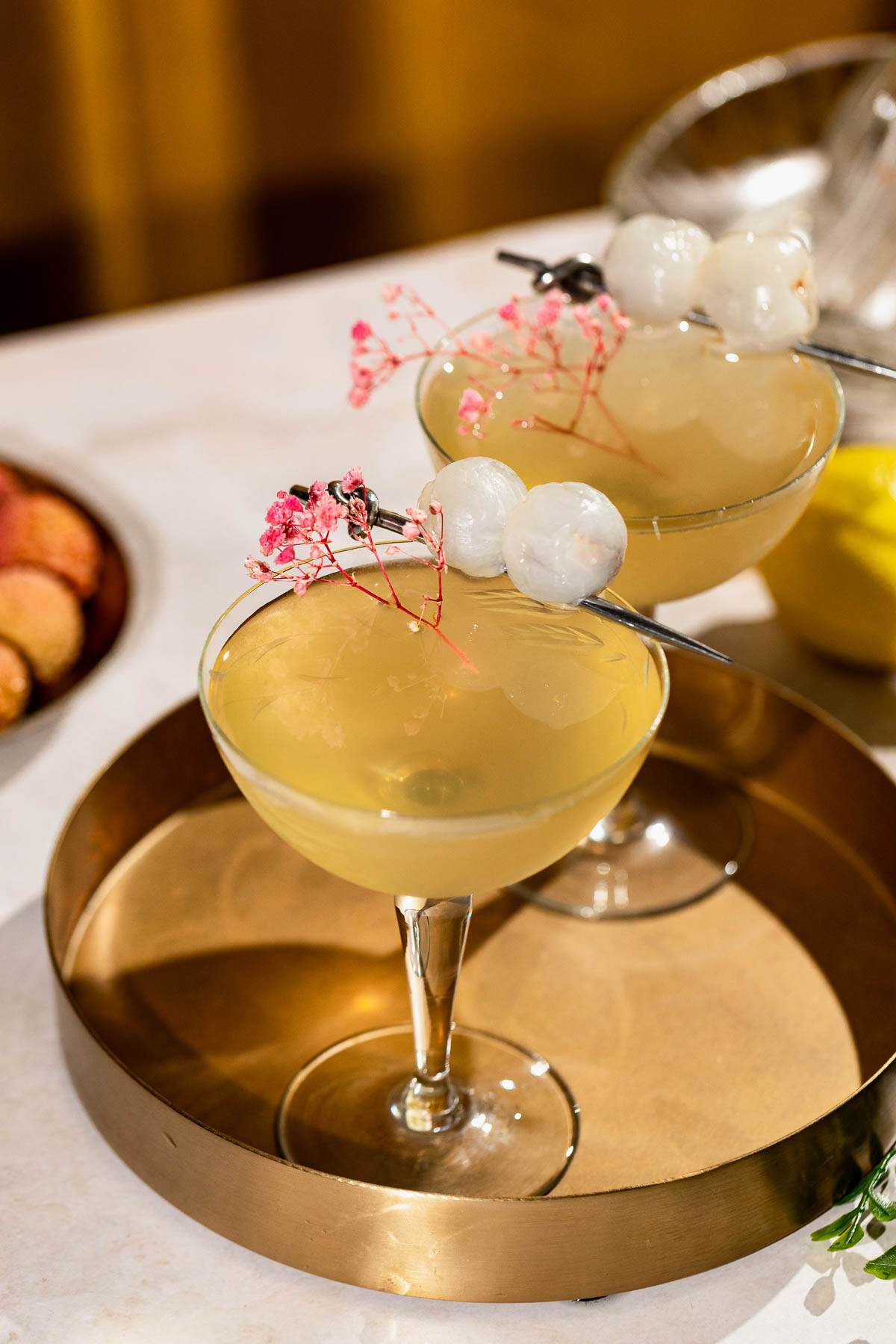Two lychee martinis with lychee garnish sit on a gold tray.