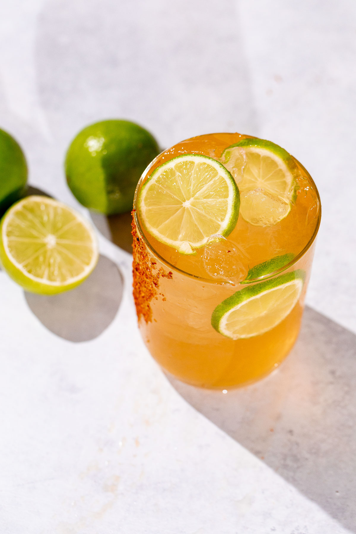 A Cadillac margarita with chili powder on the rim and lime slices, next to fresh limes on a light surface.