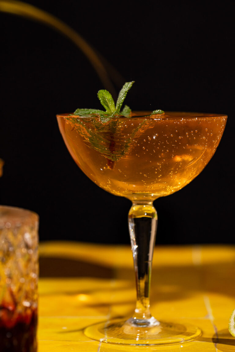 A sparkling old cuban cocktail with mint garnish sits in a coupe glass against a dark background.