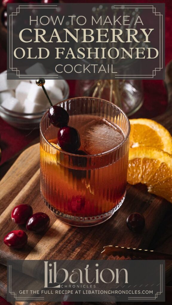 A cranberry old fashioned garnished with cranberries and orange slices rests on a wooden board with loose cranberries and sugar cubes.