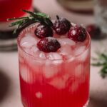 A glass of cranberry gin smash garnished with sugared cranberries and a rosemary sprig.