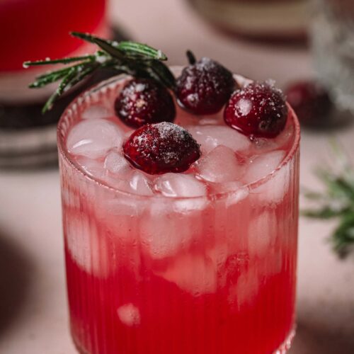 A glass of cranberry gin smash garnished with sugared cranberries and a rosemary sprig.