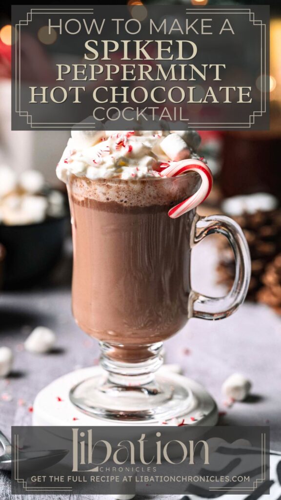 Glass mug of spiked peppermint hot chocolate with whipped cream, crushed and mini candy cane; marshmallows, pine cones behind.