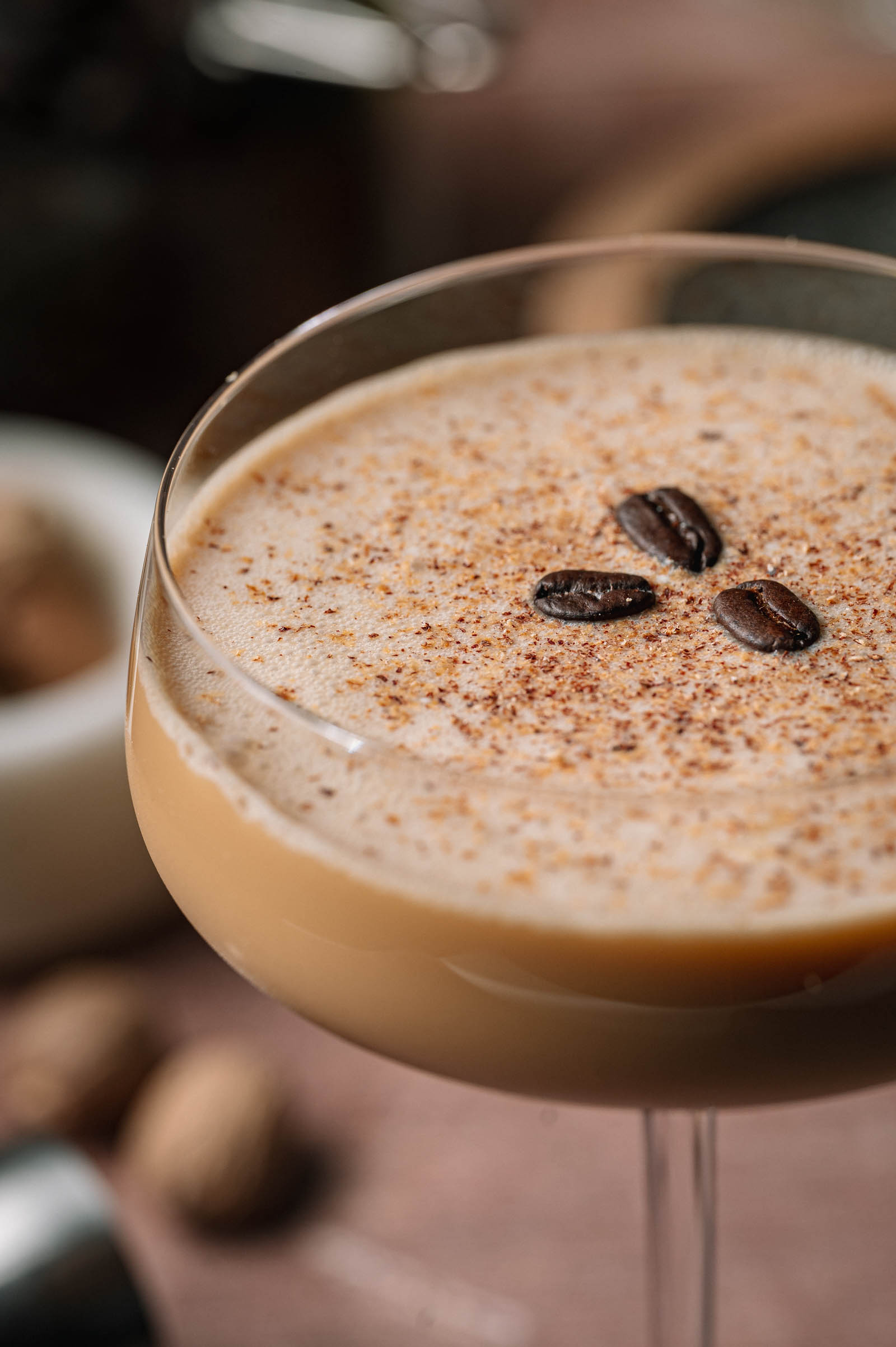Creamy coffee cocktail in a glass, topped with three coffee beans and grated nutmeg.